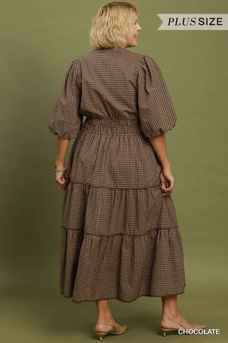 A woman shown from the back wearing a brown and black gingham tiered midi dress with puff sleeves and a smocked waist, against an olive green studio background. Text overlays read 'PLUS SIZE' and 'CHOCOLATE'.