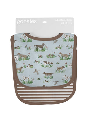 A Goosies brand adjustable bib set of two, featuring a light blue front panel with a brown and green hunting dog pattern, brown trim, and a brown striped bottom section, shown on a white background with its cardboard header.