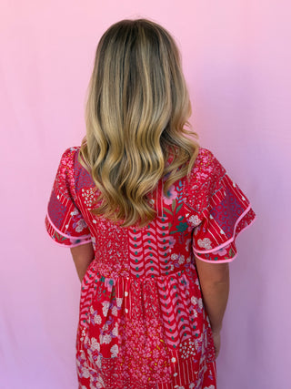 Person wearing a red floral dress against a pink background