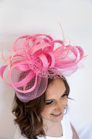 Woman wearing a large pink decorative headpiece against a white background
