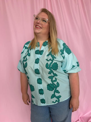 Person wearing a light blue blouse with green floral patterns against a pink background