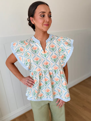 Woman wearing a floral blouse with ruffled sleeves in a room.