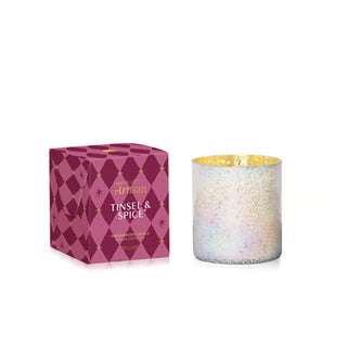 An Artisan Candle by The Candle Company in the Tinsel & Spice scent, shown with its magenta geometric-patterned packaging box and the iridescent glass candle jar with a gold glitter rim.