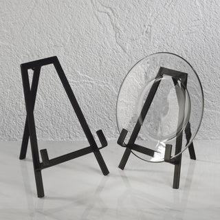 Two black metal stands with glass plates on a light gray surface and textured white wall background.