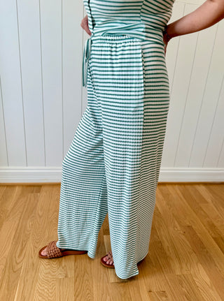 Person wearing a green and white striped outfit with wide-leg pants on a wooden floor.