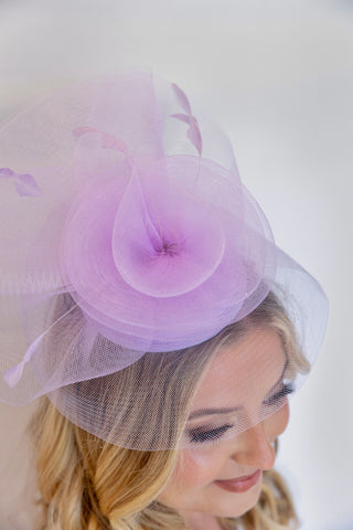 Lavender fascinator with netting on a plain background