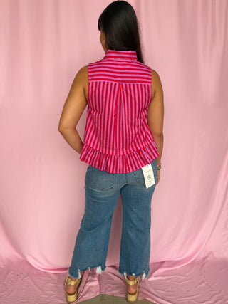 Person wearing a red and white striped sleeveless top with a peplum waist and blue jeans on a pink background.