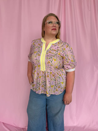 Woman wearing a floral blouse with yellow trim and blue jeans against a pink curtain background