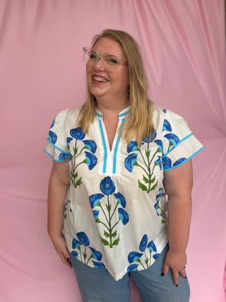 Woman wearing a white blouse with blue floral patterns against a pink background