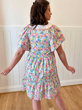 Woman wearing a floral dress against a white paneled wall.
