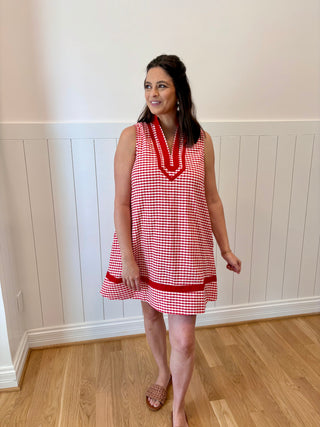 Woman wearing a red and white checkered dress standing in a room with wooden flooring and white paneled walls.