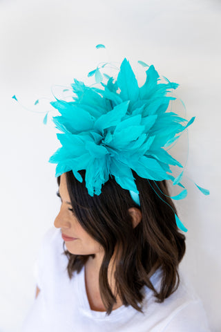 Woman wearing a turquoise feathered headpiece against a white background