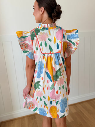 Woman wearing a colorful floral dress against a white wall.