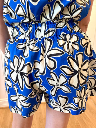 Blue romper with black and white floral pattern on a wooden floor.