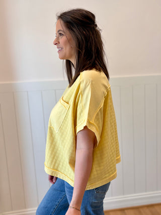 Woman wearing a yellow top and blue jeans against a white wall.