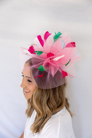 Woman wearing a decorative hat with pink and green feathers against a white background