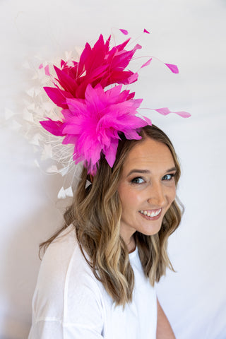 Woman wearing a large pink feathered headpiece against a white background