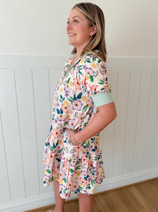 Woman wearing a floral dress standing against a white paneled wall.