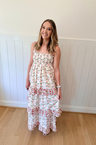 Woman wearing a floral dress and pink headpiece against a white paneled wall.