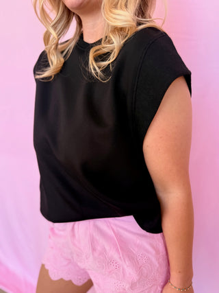 Person wearing a black top and pink shorts against a pink background