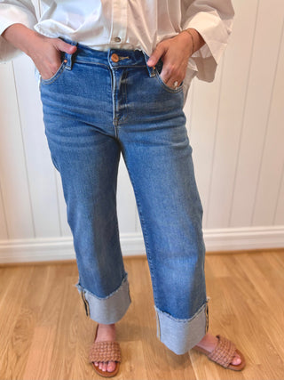 Person wearing blue jeans and a white shirt with a white paneled wall background