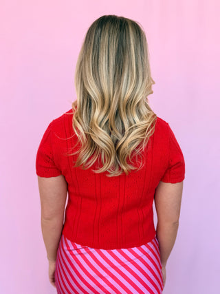 Person wearing a red sweater and pink striped skirt against a pink background