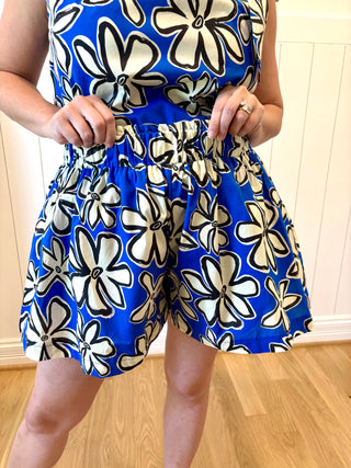 Person wearing a blue floral dress with white flowers on a wooden floor.