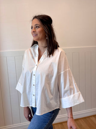 Woman wearing a white button-up shirt and blue jeans against a light-colored wall.