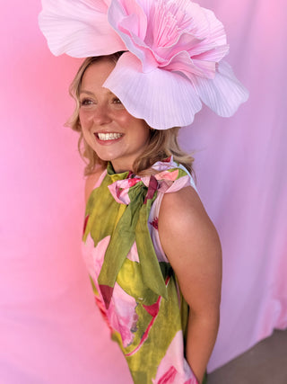 Woman wearing a large pink floral hat against a pink background