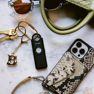 Phone case with snake skin pattern, keychain, sunglasses, and handbag on a marble surface