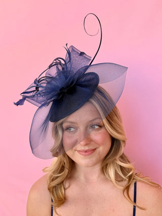 Woman wearing a navy blue decorative hat against a pink background