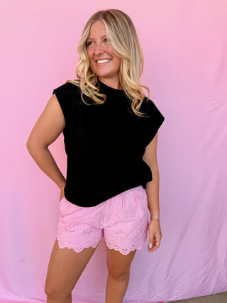 Woman wearing a black top and pink shorts against a pink background