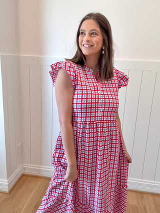 Woman wearing a red and white checkered dress standing in a room with white paneled walls.