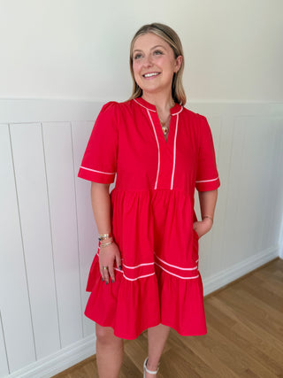 Woman wearing a red dress with white trim against a white wall.