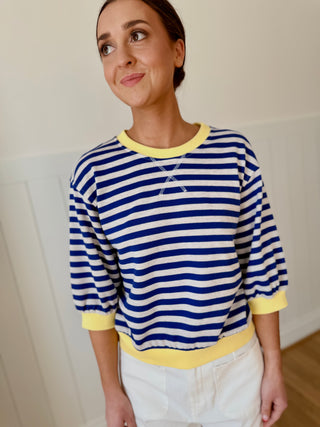 Woman wearing a blue and white striped shirt with yellow trim against a plain background