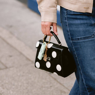 Person holding a black handbag with white polka dots on a blurred street background