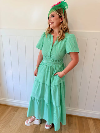 Woman wearing a green dress and headband against a white paneled wall.
