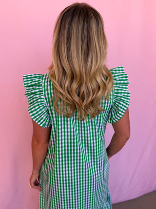 Person wearing a green checkered dress with ruffled sleeves against a pink background
