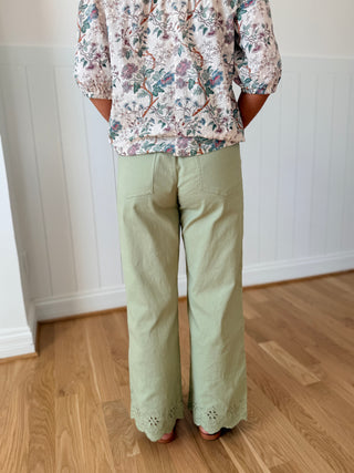 Person wearing a floral shirt and light green pants standing on a wooden floor.