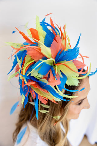 Colorful feathered headpiece worn by a person on a plain background