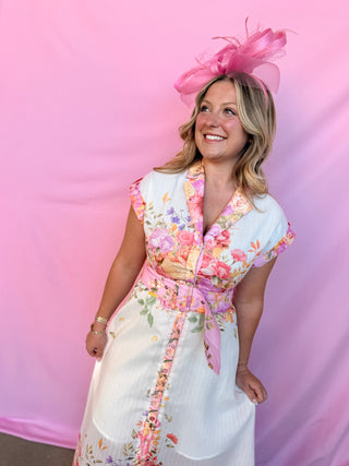 Woman wearing a floral dress and pink headpiece against a pink background