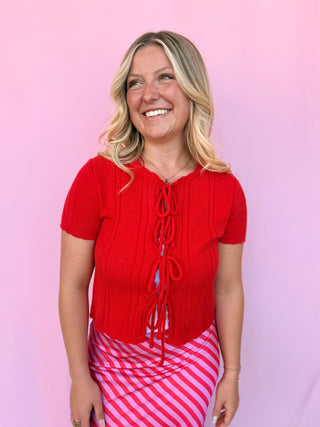 Woman wearing a red lace-up top and pink striped skirt against a pink background
