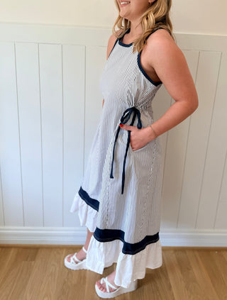 Woman wearing a white dress with black accents, standing against a white paneled wall.