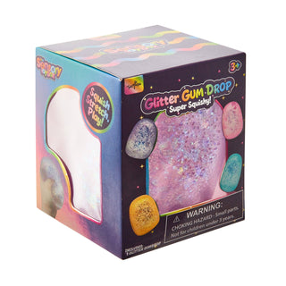A boxed toy product labeled 'Glitter Gum Drop Super Squeaky!' shown on a plain white background. The packaging is predominantly dark purple with bright rainbow graphics and a large photo of a pink glittery gum drop on the front.