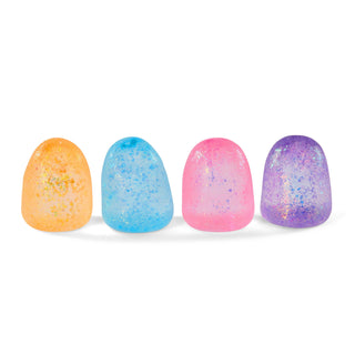 Four smooth, dome-shaped decorative stones or beads in orange, light blue, pink, and purple, each speckled with glitter, arranged in a row on a white background.