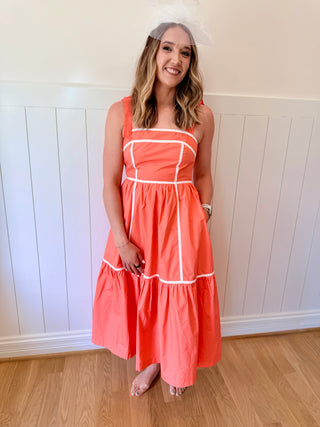 Woman wearing a coral dress with white stripes standing against a white paneled wall.