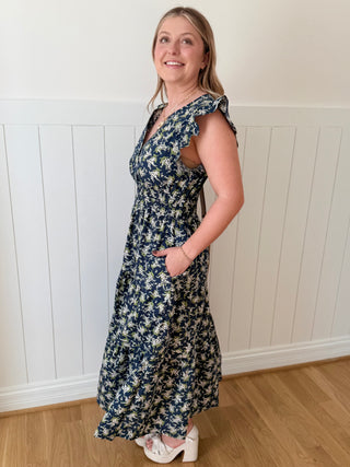 Woman wearing a floral dress standing against a white paneled wall.