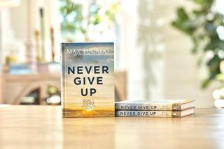 Book titled 'Never Give Up' by Max Lucado on a table with a blurred background