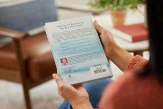 Person holding a book titled 'Stories to Remind Us We Are Not Alone' in a cozy indoor setting.