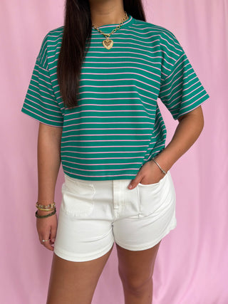 Person wearing a green and white striped shirt and white shorts against a pink background